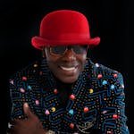 Man wearing a bold red hat with a Pac-Man patterned blazer, exuding confidence.